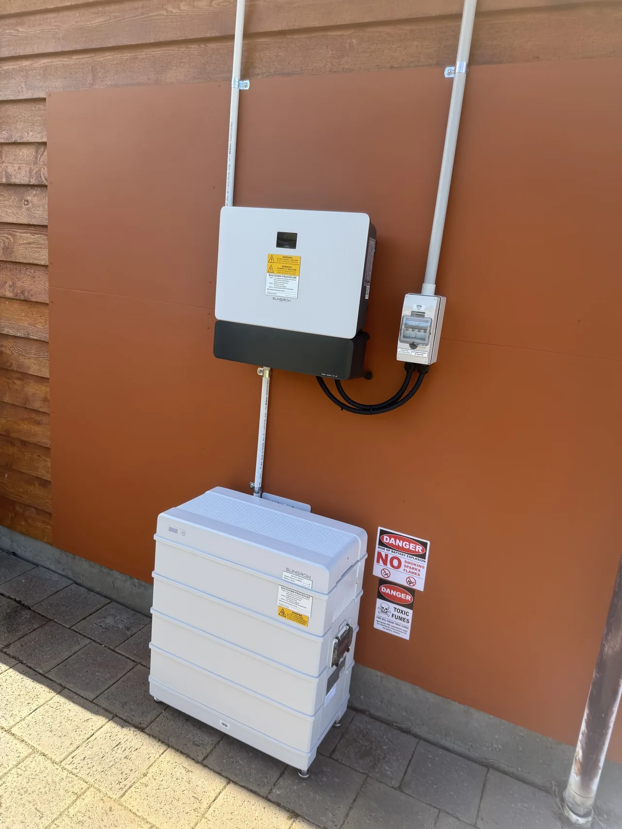 Sungrow hybrid inverter above a stacked battery cabinet against a rust-red wall