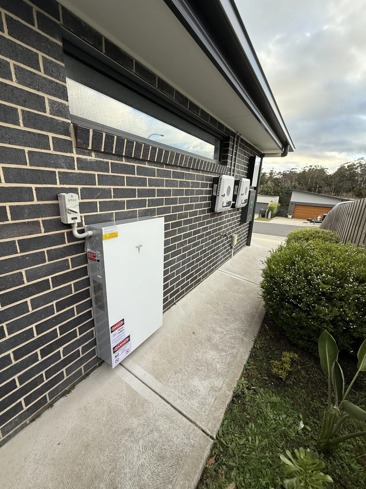 The Powerwall being positioned against the brick wall beside the existing inverters
