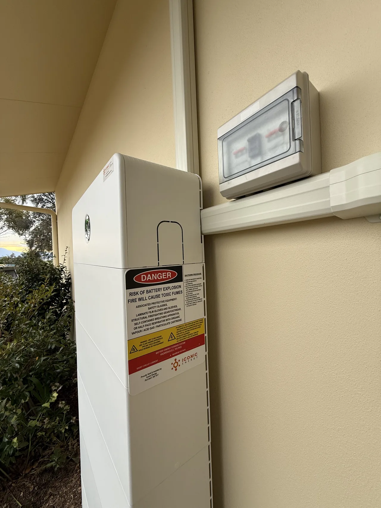 Top of the battery cabinet showing its safety labelling, with the isolator enclosure mounted on the wall beside it
