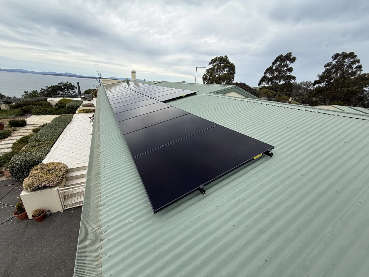 Black solar panels installed along a green metal roof at a Sandford home, with the water in the background